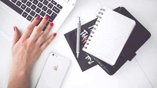 Women hand working on laptop with phone and notepad kept on table