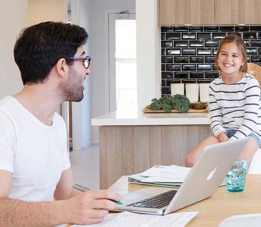 Small girl smiling at her father while working on his laptop