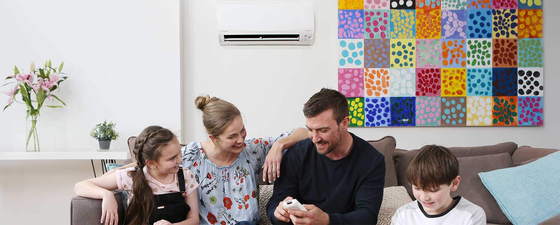 Family sitting on sofa and using remote controller of Air conditioner installed on the wall